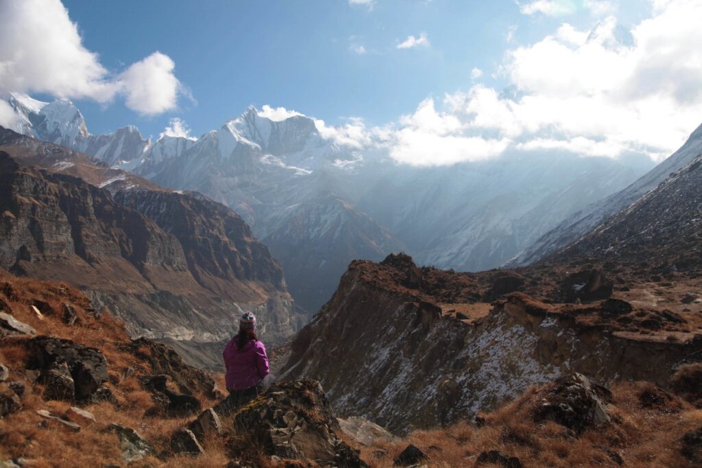 Solo hiker admiring snow-covered mountains from a viewpoint along the Annapurna Base Camp trail.