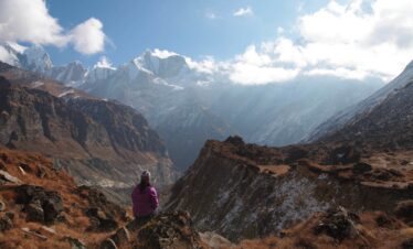 Solo hiker admiring snow-covered mountains from a viewpoint along the Annapurna Base Camp trail.