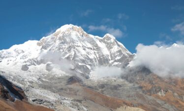 Panoramic view of the Annapurna mountain range from the base camp at sunrise, with golden light on the snowy summits.
