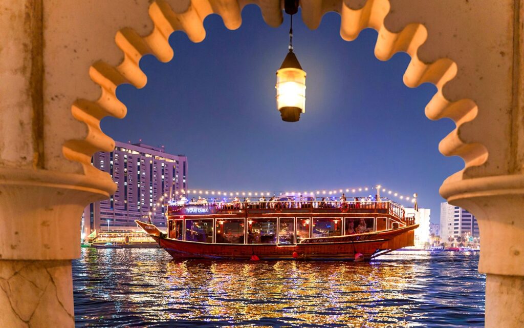 Traditional wooden dhow boat sailing on Dubai Creek during evening cruise